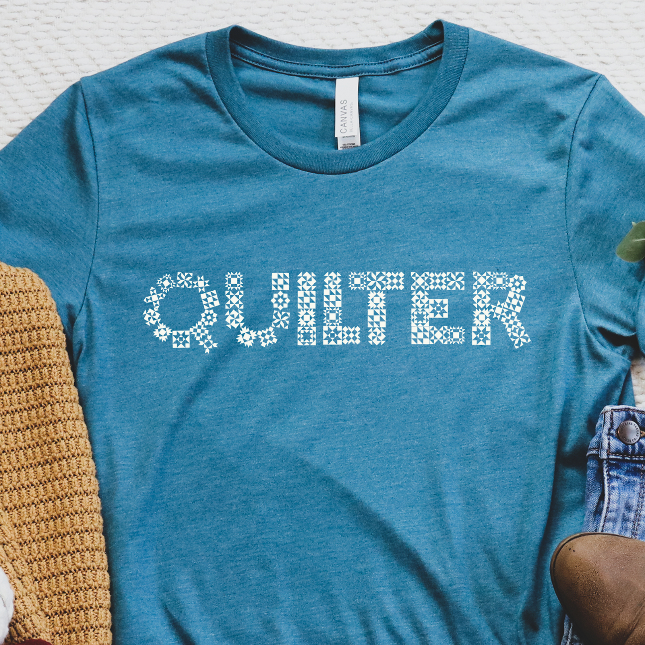 Blue t-shirt with 'QUILTER' text, surrounded by autumn-themed items on a textured surface.